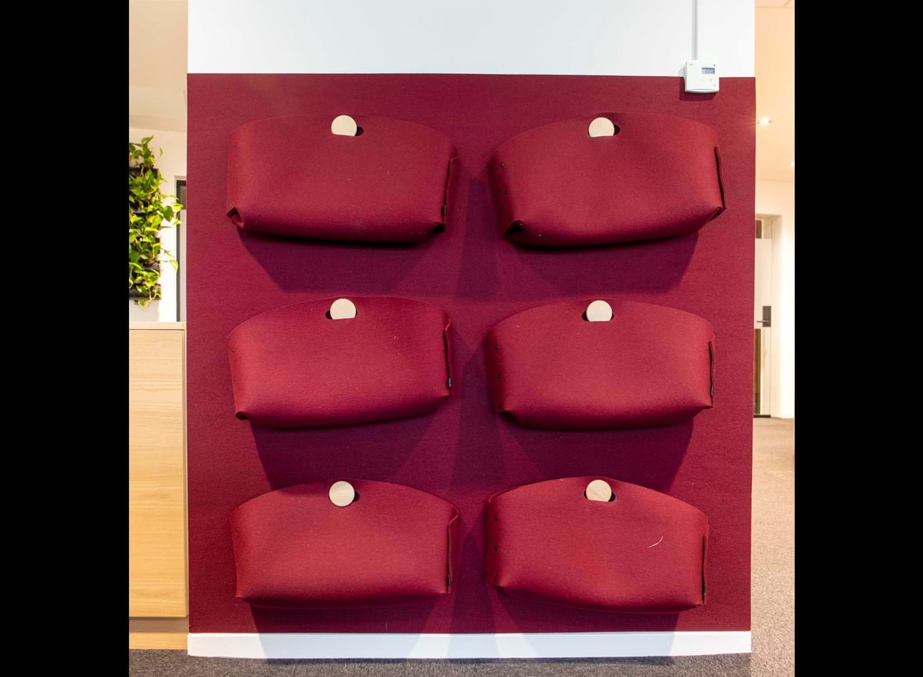 6 røde kontortasker i filt ophængt på væg